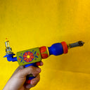 Colorful wooden toy radar gun held by a hand against a yellow background