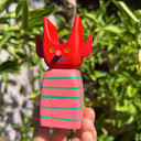 Colorful wooden toy figure with a red, cute devil character with a striped body on a yellow background