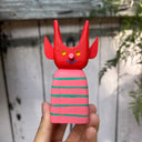 Colorful wooden toy figure with a red, cute devil character with a striped body on a yellow background