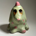 Ceramic dog like creature with green skin and pink polka dots on a neutral background