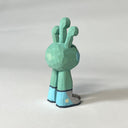 Mint green whittled wooden sculptures of a space alien, with 3 eyes and 2 legs without any other body features. It smiles with buck teeth and wears shiny silver shoes.