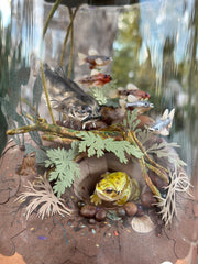 Mixed media diorama of an underwater scene, with a large scary looking fish swimming over a mound of land. Burrowed into the side of the mound is a small frog, hiding from the fish.