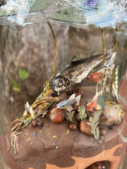 Mixed media diorama of an underwater scene, with a large scary looking fish swimming over a mound of land. Burrowed into the side of the mound is a small frog, hiding from the fish.