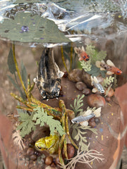 Mixed media diorama of an underwater scene, with a large scary looking fish swimming over a mound of land. Burrowed into the side of the mound is a small frog, hiding from the fish.