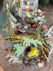 Mixed media diorama of an underwater scene, with a large scary looking fish swimming over a mound of land. Burrowed into the side of the mound is a small frog, hiding from the fish.