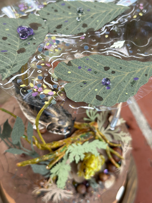 Mixed media diorama of an underwater scene, with a large scary looking fish swimming over a mound of land. Burrowed into the side of the mound is a small frog, hiding from the fish.