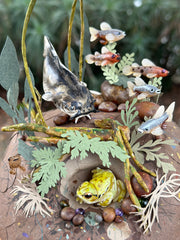 Mixed media diorama of an underwater scene, with a large scary looking fish swimming over a mound of land. Burrowed into the side of the mound is a small frog, hiding from the fish.