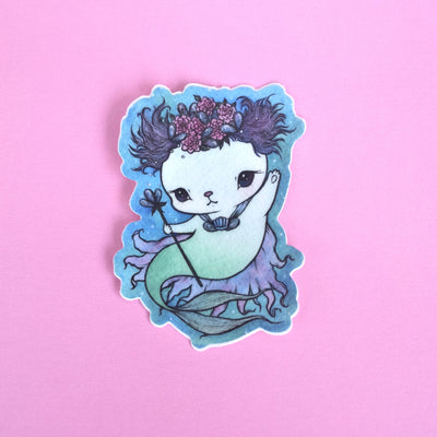 Die cut sticker of a cat mermaid, with flowing purple hair and a shell shaped scepter.