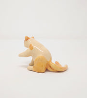 Small ceramic sculpture of a 2-tailed cream colored cat with orange color accents. It sits on its hind legs with one paw extended out.