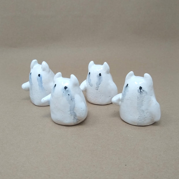 4 small white ceramic ghosts with little devil horns, all crying watercolor tears. They have no facial features other than black eyes and minimal body features, only one arm that extends outwards.