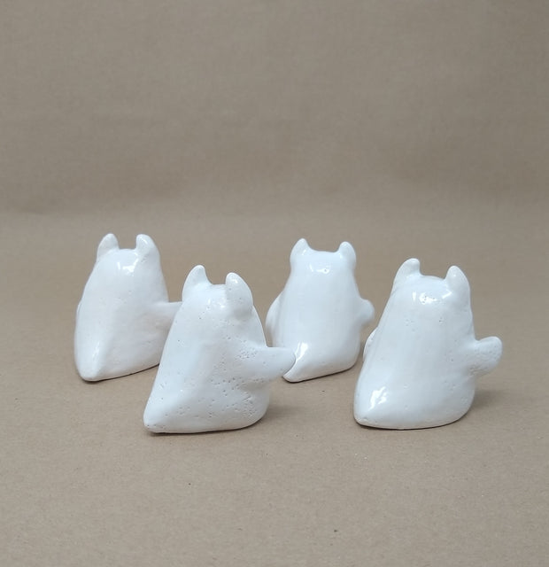 4 small white ceramic ghosts with little devil horns. They have no facial features other than black eyes and minimal body features, only one arm that extends outwards.