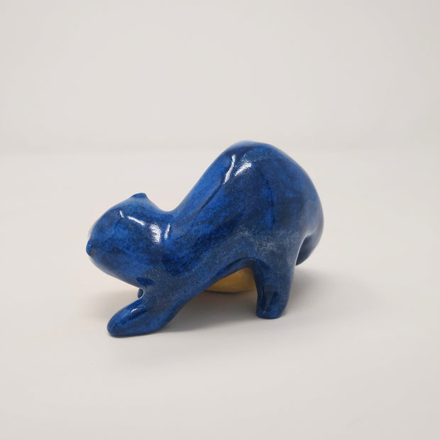 Ceramic sculpture of a blue otter, with its body positioned atop of a yellow gourd. Back angle, to show the otter with a front and back paw on the ground.