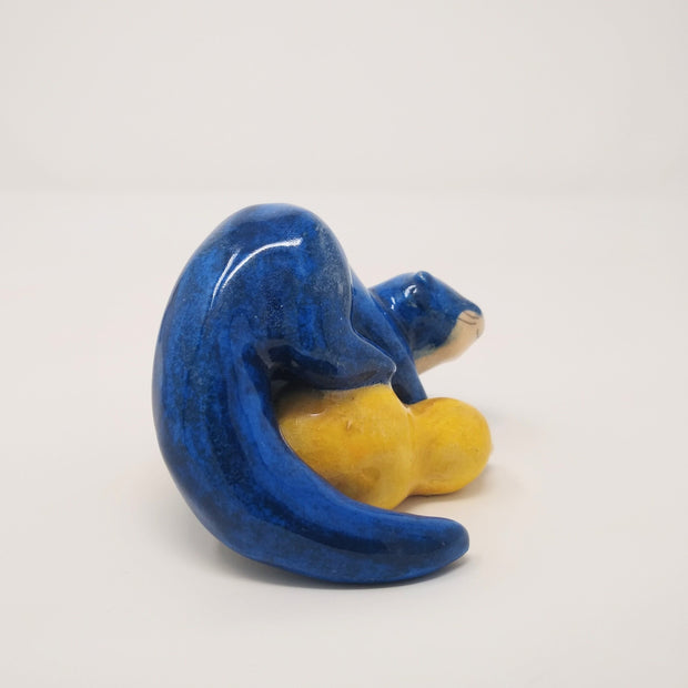 Ceramic sculpture of a blue otter, with its body positioned atop of a yellow gourd. 
