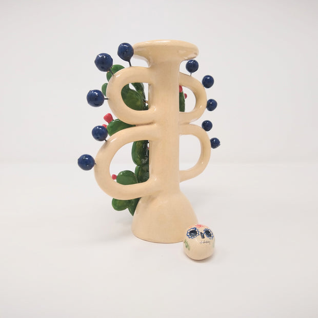 Back view of ceramic sculpture, only the cream colored base with blue spheres protruding remaining. A painted skull sits at the bottom.