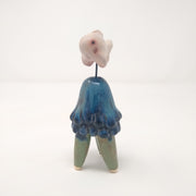 Ceramic sculpture of a blue jellyfish like creature, with 3 legs like a table. Mounted above it via a wire is a white fish, akin to a goldfish.