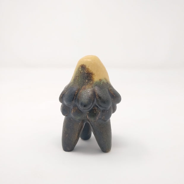 Ceramic sculpture of a small jellyfish creature, with 3 legs like a table. It is mostly grey with a tan coloring at the top.
