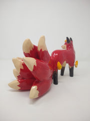 Glossy ceramic sculpture of a red fox with a large tail, composed of 9 different smaller tails. The fox has a small golden horn and some gold flames come of its body.