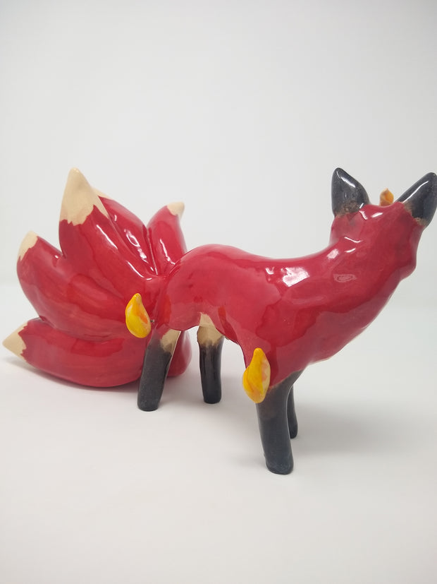 Glossy ceramic sculpture of a red fox with a large tail, composed of 9 different smaller tails. The fox has a small golden horn and some gold flames come of its body.