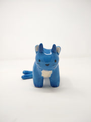 Small blue ceramic sculpture of a cat with 2 tails and horns coming out atop its head. It has simplistic body features and a drawn on face.