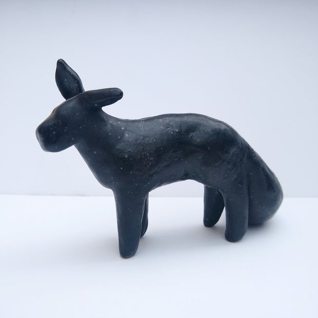 Dark blue sculpture of a fox like animal, with pointed ears and a large bushy tail. It has no facial features and its body shapes are minimally rendered.