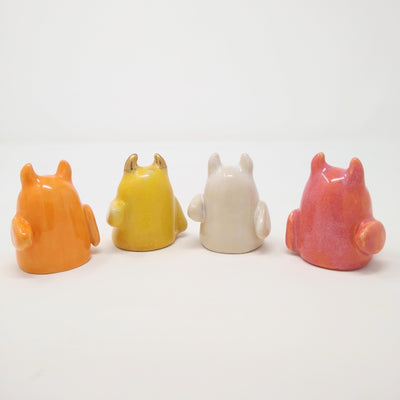 4 ceramic figures of round bodied ghosts with devil horns and small arms. No facial features have been defined. Colors are: orange, yellow with gold horns, white and red.