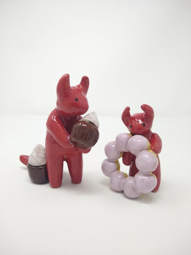 Pair of 2 small devil sculptures. One holds a cupcake and the other holds a large mochi donut.