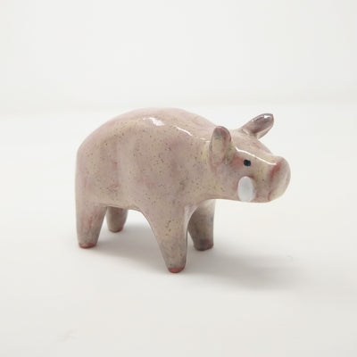 Ceramic sculpture of a light pinkish tan colored boar, with drawn on eyes and white tusks. It stands with a slightly hunched back.