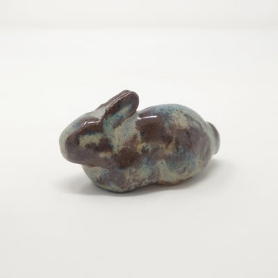 Sculpture of a brown and light tan/blue speckled bunny, in "loaf" position. It has no facial features and minimalistic body features, aside from a round tail.