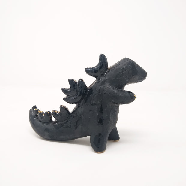 Ceramic sculpture of a dark blue abstract Godzilla figure, with abstract spikes on its back, no facial features, and one arm extended out.