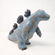 Ceramic sculpture of a brown and blue abstract Godzilla figure, with abstract dark blue spikes on its back, no facial features, and one arm extended out in front.