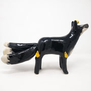 Ceramic sculpture of a black fox with white chest and tail tips. The fox has 3 tails and small golden flames coming off its head and legs.