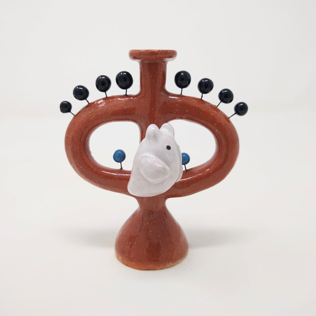  Ceramic sculpture of a brown vessel with handles and a small flat area up top. A white ghost with small devil horns is on the front of the sculpture. Small black balls come out of the vessel via wire.