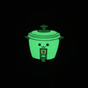 Die cut enamel pin of a rice cooker, with a small simple set of eyes and a cute smile. Pin is glowing in the dark.
