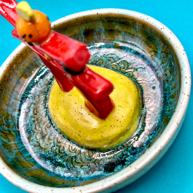 Ceramic sculpture of a red gate with a small orange citrus on top, within a ceramic bowl.