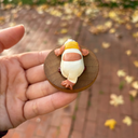 Small figurine of a dog on a wooden base held in a hand with a blurred outdoor background.
