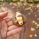 Hand holding a small figurine of a dog with blonde hair and a white outfit on a blurred outdoor background.