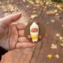 Hand holding a small figurine of a dog character with a round base on a brick path with fallen leaves.