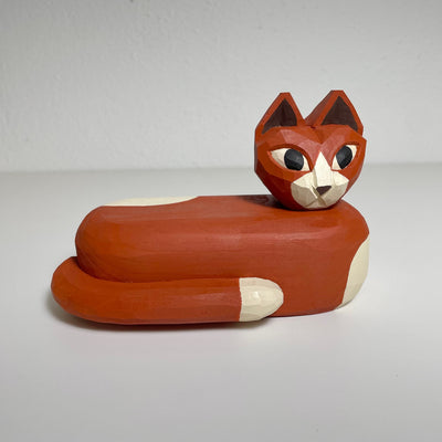 Carved and painted wooden sculpture of a orange brown cat with white spots, curled up into itself with its head popping out. 