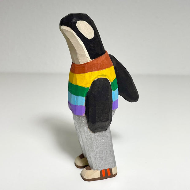 Carved and painted wooden sculpture of an orca standing on 2 legs like a person. It wears a rainbow striped shirt, grey pants and sneakers.