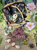 Diorama made of clay and paper of a character napping in a wooden structure in a tree, alongside a napping raccoon. Around them are flowers and a tiny hedgehog family with 3 babies.