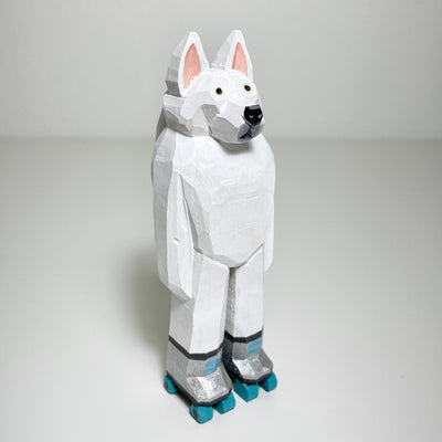 Carved and painted wooden sculpture of a fluffy white dog, like a husky, standing on 2 legs like a person. It wears a pair of silver roller skates with teal wheels. 