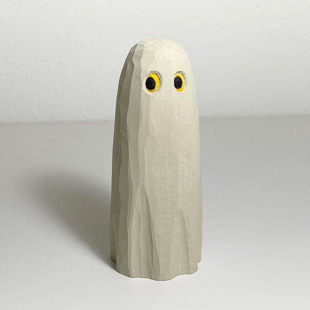 Whittled and painted wooden sculpture of a ghost, cream colored with bright yellow eyes shining under the sheet and looking to the side. Ghost has no other facial or body features.