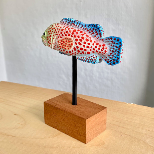 Sculpture of a spotted grouper fish, with bright red dots, blue coloring on its tail/fins and a light green coloring around the face.