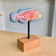 Sculpture of a spotted grouper fish, with bright red dots, blue coloring on its tail/fins and a light green coloring around the face.