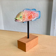 Sculpture of a spotted grouper fish, with bright red dots, blue coloring on its tail/fins and a light green coloring around the face.