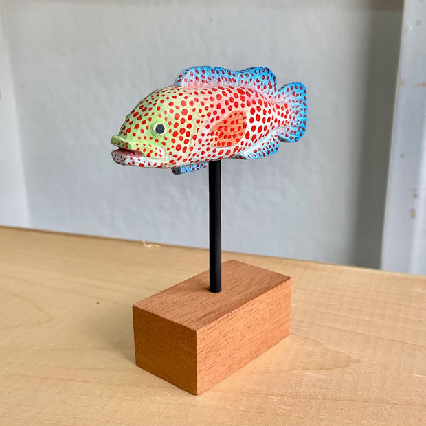 Sculpture of a spotted grouper fish, with bright red dots, blue coloring on its tail/fins and a light green coloring around the face.