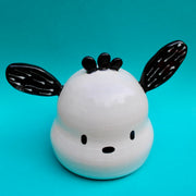 Ceramic sculpture of a white dog head made to look like Sanrio's Pochacco with black pointed in different directions.