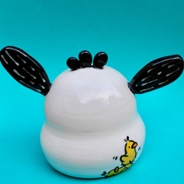 Ceramic sculpture of a white dog head made to look like Sanrio's Pochacco, seen from the back with a drawing of 2 small ducks playing.