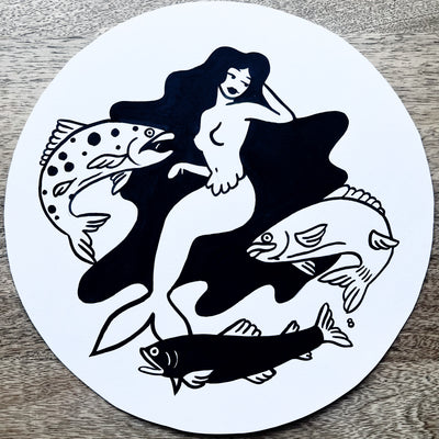 Black ink line drawing on white circular paper of a mermaid with very long black hair. 3 fish, akin to salmon, swim around her.