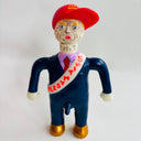 Toy figure of a person wearing a red cap and blue suit with a sash on a white background